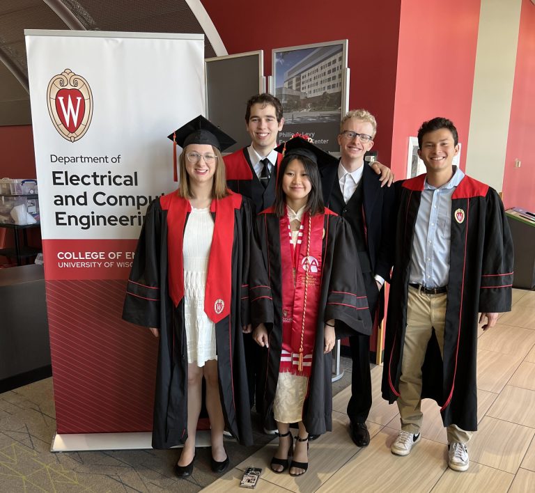 Five students wearing black graduation gowns standing next to a pull up banner that reads Department of Electrical and Computer Engineering